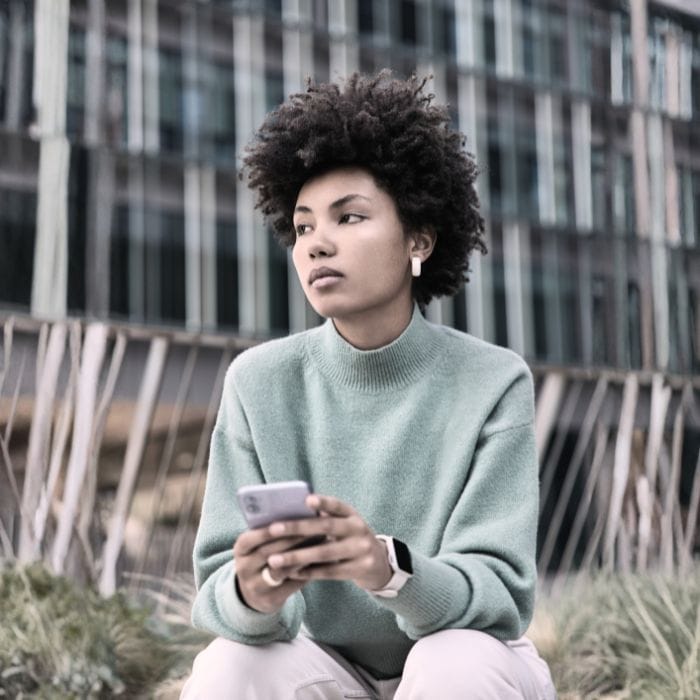 A woman sitting alone with her phone representing the distance and confusion that situationships can cause.